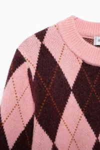 Detailopname van een roze en donkerbruine argyle gebreide truidetails met geribbelde ronde hals.