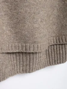 Close up detail of womens knitted cape hem, textured ribbed knit fabric, elegant design.