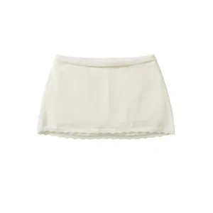 Close-up detail shot of the white knitted mini skirt featuring a delicate scalloped hem.
