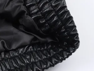 Close-up detail of black leather jacket fabric texture and elastic hem design for women.