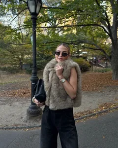 Outdoor street fashion detail showing a stylish faux fur vest in autumn park setting.