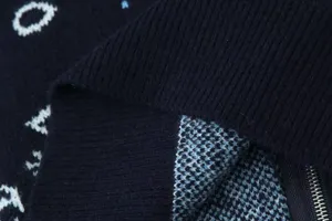 Close-up detail of dark blue knitted cardigan fabric with white jacquard letters and zipper.