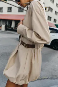 Primo piano dettagliato di un abito beige a maniche lunghe con elegante cintura marrone.
