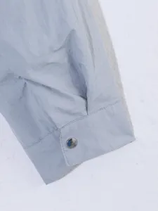 Detalle de primer plano del puño de manga de chaqueta de mujer azul claro con botón metálico.