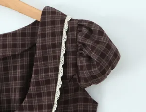 Gros plan sur les détails de la robe à carreaux marron, col en dentelle et manches bouffantes.