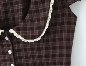 Détail d'une robe à carreaux marron avec un col claudine en dentelle blanche et boutons.