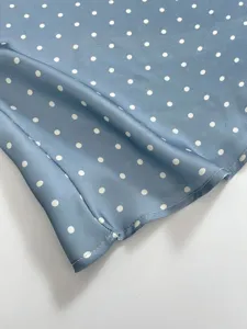 Close-up view of blue satin fabric with white polka dots, soft drape and smooth texture.