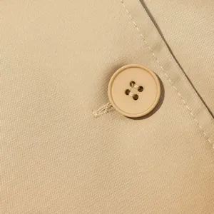 Primer plano de detalle de tela de chaqueta corta caqui con botón a juego y costuras finas.