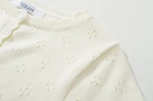 Close-up detail shot of white knitted summer top featuring delicate hollow-out pattern.