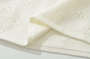 Detail shot of breathable pointelle knit fabric texture in soft off-white color.