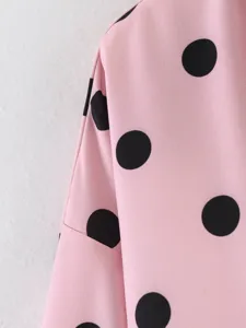 Primo piano dettagliato di camicia rosa a maniche lunghe con pois neri classici eleganti.