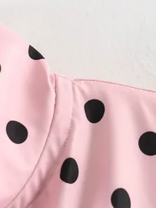 Primo piano dettagliato di una blusa rosa a pois neri, con cuciture fini e trama del tessuto.