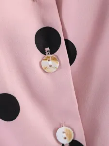 Dettaglio camicia a pois rosa e neri, primo piano su bottone marmorizzato e tessuto fine.