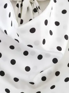 Tejido efecto seda con lunares negros y detalle elegante de cuello drapeado.