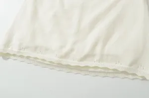 Detailed view of white knitwear hem, breathable summer clothing, elegant scalloped trim.