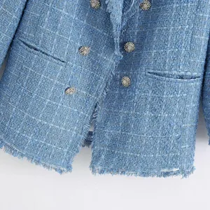 Close-up detail of women's blue tweed blazer jacket, textured fabric with fringe edge buttons.