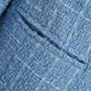 Close-up detail of blue tweed fabric jacket pocket, showing fine woven texture and craftsmanship.