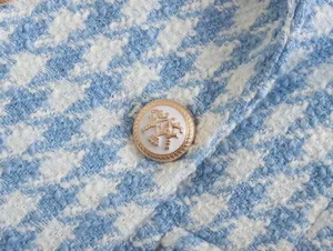 Close-up detail of light blue houndstooth tweed fabric featuring a decorative gold and white button.
