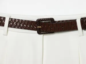 Detail shot of women's brown embossed belt and white high-waisted pleated shorts waist.
