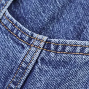 Λεπτομερής όψη μπλε denim υφάσματος με ραφές αντίθεσης, που δείχνει εξαιρετική ποιότητα.