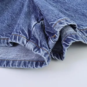 Λεπτομερής κοντινή λήψη μπλε τζιν υφάσματος με κλασικές κίτρινες ραφές και φυσικές πτυχές.