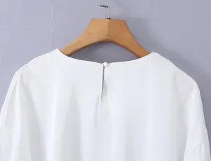 Detail view of a solid white round neck long sleeve top hanging on a wooden hanger.