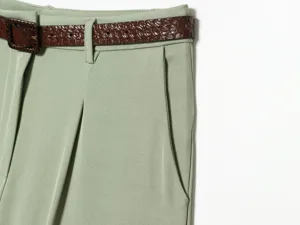 Close-up of green pleated high-waisted shorts detail featuring a brown textured belt.