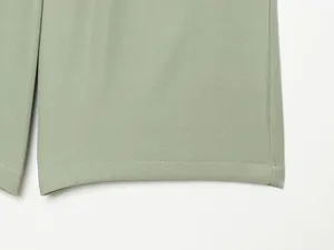 Green shorts fabric hem close-up, showing fine twill texture and neat stitching details.