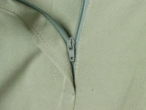 Close-up detail of the metal zipper and fine stitching on the minimalist green shorts.