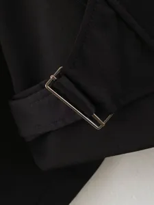Close-up detail of black jacket featuring stylish metal buckle strap and neat fabric stitching.