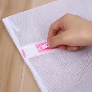 Gros plan d'un sac à linge en filet blanc avec fermeture éclair rose, texture fine.