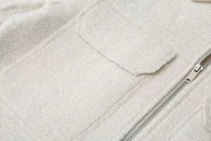 Close-up of white textured jacket detail featuring front zipper and chest pocket design.