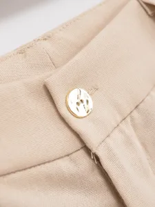Close-up detail shot of women's elegant beige pants waistband with metallic gold button.