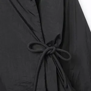 Detalle de abrigo kimono negro, elegante cinturón de lazo y tela texturizada para otoño.