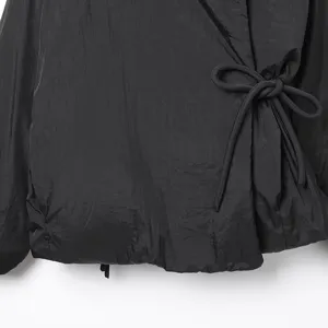 Primer plano de la chaqueta kimono acolchada negra para mujer con detalle de lazo y tela suave.