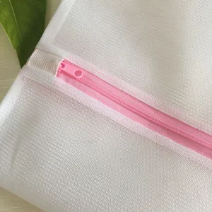 Détail de sac à linge en maille blanche, tissu fin avec fermeture éclair rose et protection.