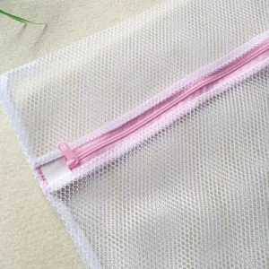 Gros plan sur le sac a linge en maille blanche avec fermeture eclair rose, filet delicat.