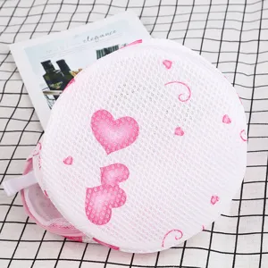 Cylindrical mesh laundry bag with pink heart pattern for bra protection and washing machine.
