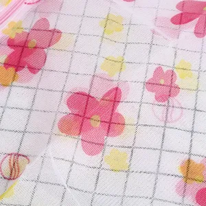 Gros plan du sac à linge en filet, délicat imprimé floral rose et jaune et texture quadrillée.