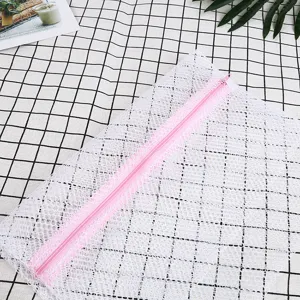 Vista detallada de bolsa de malla blanca para lavadora con cremallera rosa, duradera y práctica.