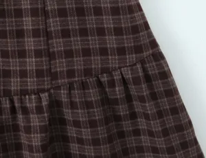 Gros plan détail du tissu de robe à carreaux marron rétro avec texture plissée chic.