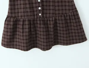 Detail de robe carreaux marron avec motif vintage, boutons blancs et bas volant.