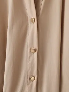 Dettaglio bottone abito manica lunga beige, trama fine con eleganti bottoni metallici dorati.