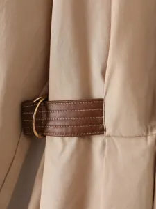 Primo piano della cintura in vita del trench da donna con dettaglio di anello in metallo.