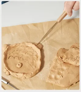 Detailaufnahme von Ton-Schnitzwerkzeugen, die Hand beim Modellieren von Ton mit Holzgriff zeigen.