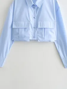 Light blue cropped long sleeve shirt detail, featuring classic lapel collar and dual chest pockets.