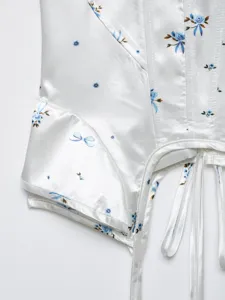 Close-up detail of white satin floral corset top with boning structure and delicate blue print.