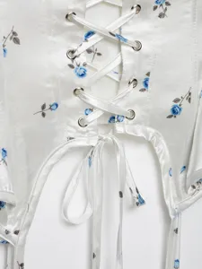 Close-up of white satin floral lace-up camisole top with metal grommets and ribbons.