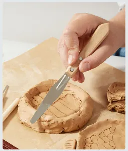 Primer plano de la herramienta de escultura de arcilla con mango de madera moldeando arcilla.