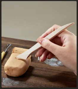 Detail shot of wooden clay sculpting tool in use, hand carving pottery on table surface.